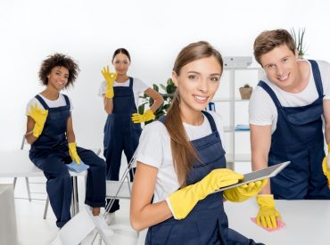 smiling young female cleaner using digital tablet while colleagues working behind